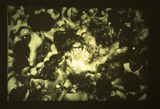 An old image showing people closely packed together, with two figures at the center illuminated by another image overlaid. 