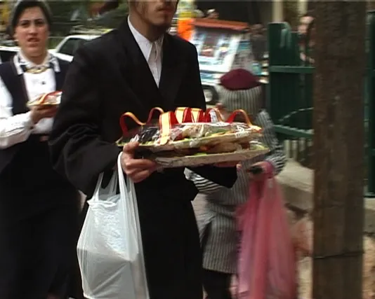 Fancy dressed adults on a street carry decorative trays of offerings wrapped in red and gold ribbon for the feast of Purim. 