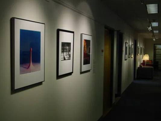 A dim hallway with multiple offices exhibits photographs. Each is individually lit and shown at the same height.