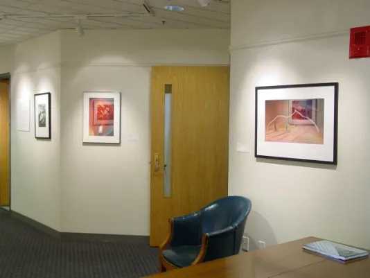 A seating area with a table and chair sit outside of offices in the hallway. Above them are photographs hung in a row.