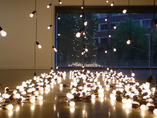 Strands of white lights hang from the ceiling and lie grouped together on the gallery floor, reflecting in a large window.