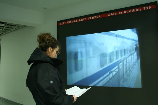 A visitor reads a pamphlet in front of video projection in a hallway showing a blurry view of a train in motion.