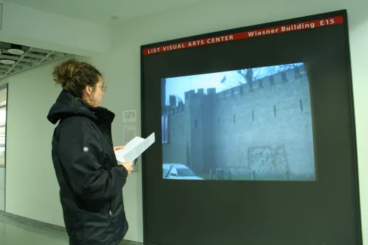 A visitor stands in front of video projection in a hallway showing a structure that has walls like a castle.