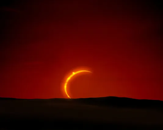 A sliver of yellow sun is visible against an orange, red sky with a dark shadowed landscape directly below.