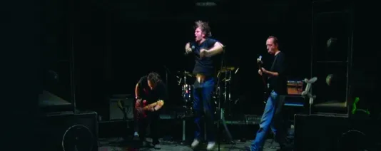 A still of 3 men performing in a band - two playing guitar and one person singing 