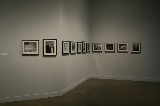 A series of black and white photographs hang together on three angled walls.