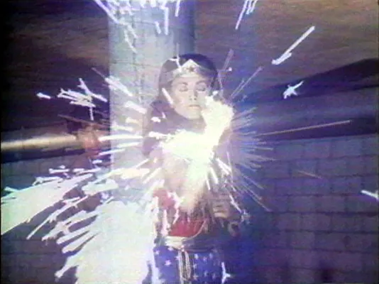 Video still of wonder woman running in a hallway with fireworks in the foreground. 
