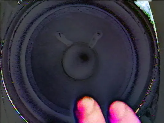 A blurry still of a hand lightly pressed against the head of a speaker.