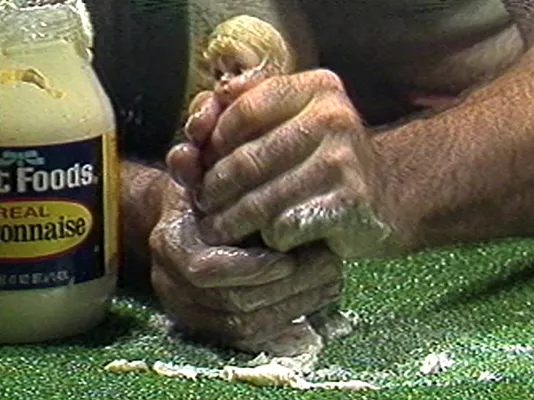 Close view of hands squeezing a small doll with mayonaise. 