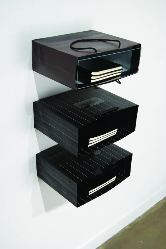 Three rectangular black paper bags attached to the wall like shelves in a vertical column, each holding several notebooks