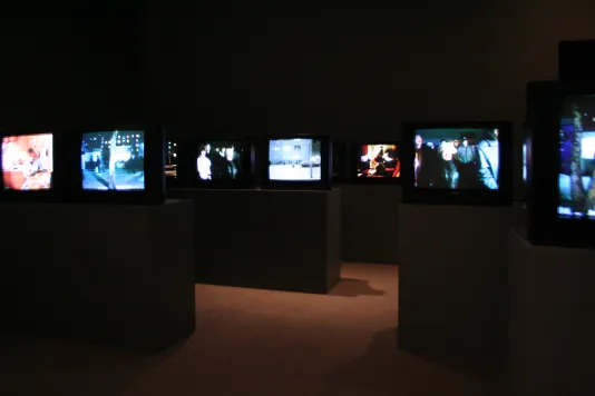 Many screens installed on podiums in a darkened gallery. 