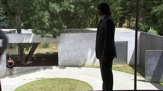 A man in a suit standing in a park like setting.