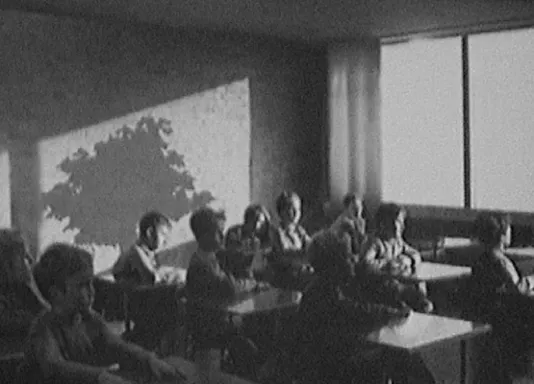 A black and white photo of students in a classroom sitting at individual desks. 