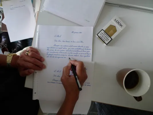 A hand writing and a letter are in frame.