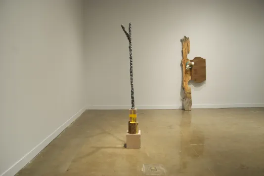 A forked stick sculpture standing upright on a base of three cubes, a wood sculpture with objects attached, leaning on a wall