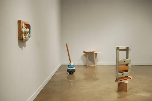 Four sculptures, one on a wall, one against the other wall, one on a plinth, and a ceramic urn with a tube jutting out the top