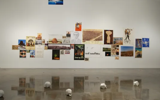 A large collage with colorful pages and pictures on the back wall, and five white skull forms on the floor in the foreground