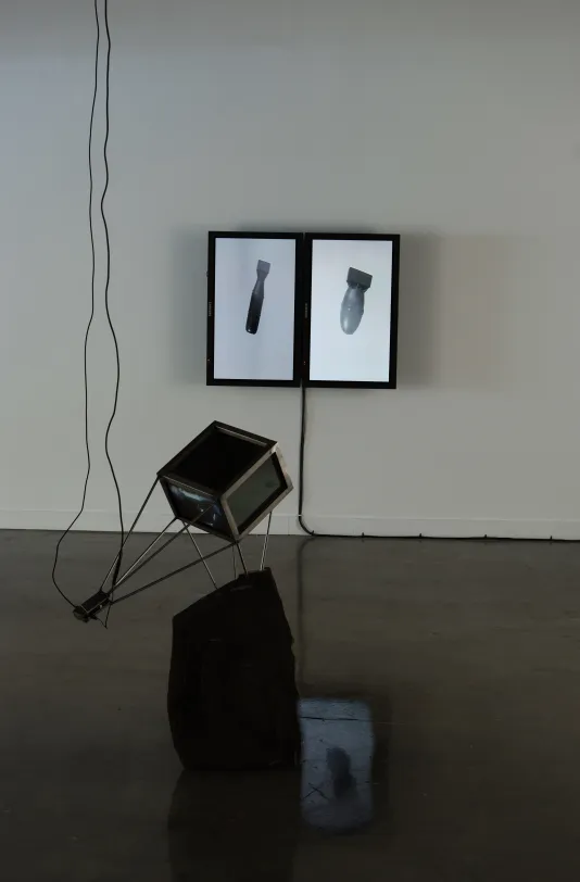A two panel monitor sculpture each with an image of a bomb floating in the space, and a box like piece with wires going up