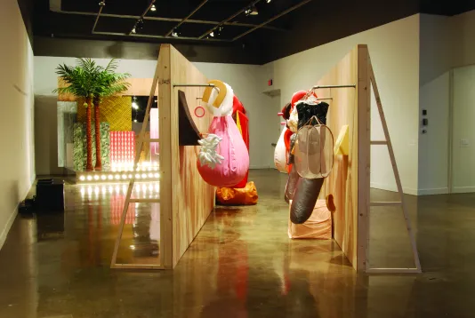 Two facing moveable walls with colorful props hanging from racks, and a set w lights, fake palm trees, a red and white panel