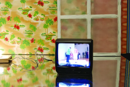 Wallpaper with red flowers and palm trees, a leaning window, and a video monitor with an image that looks like a performance
