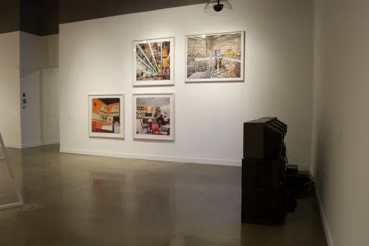Four colorful framed photographs with lots of orange, and a side view of two video monitors on the floor