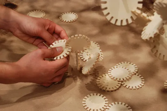 Hands connect the notches around the edges of flat round discs to form 3-dimensional structures.