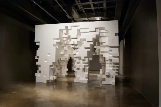 Cube-like structure made from white Styrofoam blocks and blocks removed to form irregular-shaped arch openings and footings