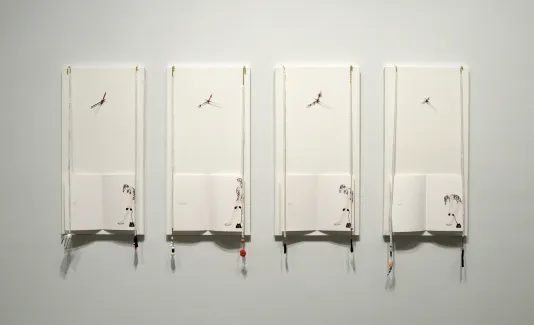 Four white panels hang against the wall. At the bottom, an open book with an illustration of a woman slumped over.