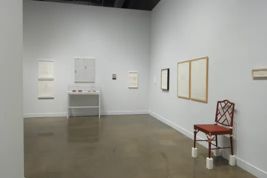 Installation view of the List Center gallery with work by Frances Stark hanging on the walls. In the foregound is a red chair standing on stilts.