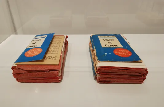 Two copies of Henry Miller's "Tropic of Cancer" sit side by side. They are both well worn and filled with red note cards indicating annotations. 