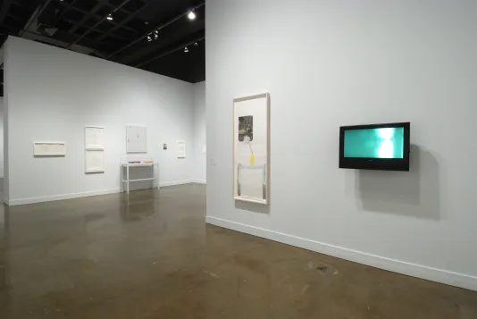 Installation view of the List Center gallery with a mix of collages, video screens, and photographs, all framed with light wood and white frames.