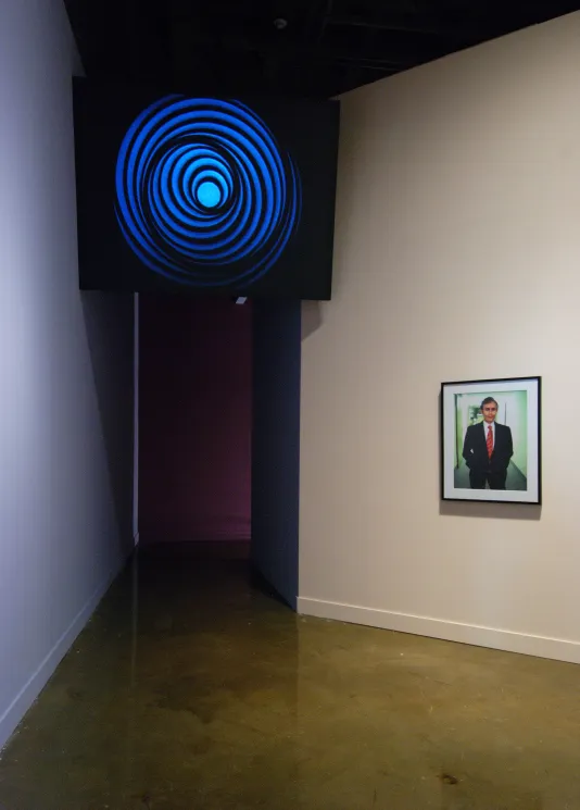 An angled wall above a dim hallway shows an image of a blue spiral shape, a color photo is hung on a wall to the right.