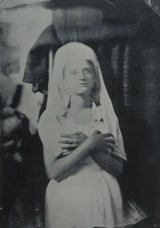 Black and white image of a young woman in white veil and dress with her gaze upward and arms crossed against her chest