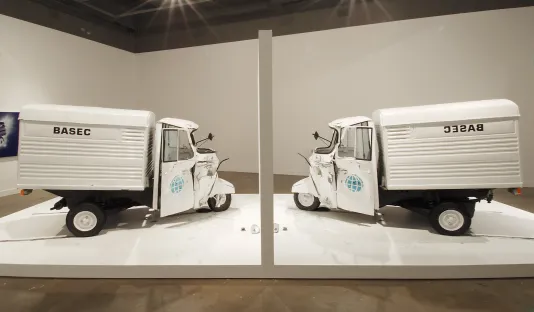 2 white vehicles named “BASEC” and reversed “CESAB” face one another on either side of a white display wall and platform.