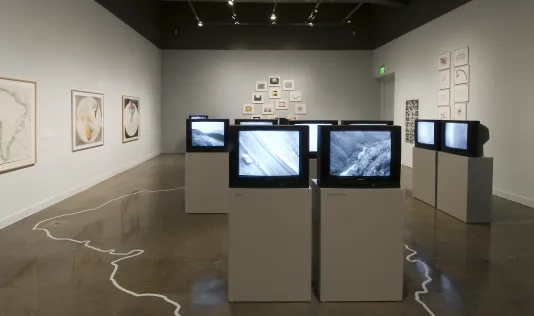 Installation showing many TV monitors and art on the surrounding walls. 
