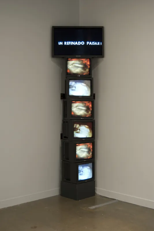 A tower of 6 TV monitors with a large TV on the top with the words UN REFINADO PAISAJE II