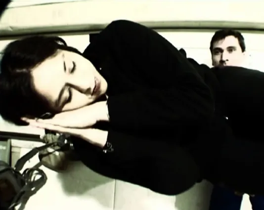 A single frame with a woman lying on her side, eyes closed, hands under her head, a man standing behind her