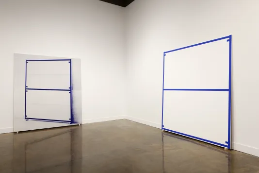 A canvas edged and bisected with a blue line and a screened image of that canvas lean against perpendicular walls.