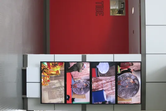 Four video monitors, displaying 4 different colorful scenes, are stacked together on a gridded wall next to a red alcove.