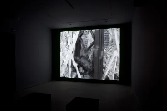 A monochromatic image of trussed industrial columns against a cityscape, projected on a wall in a dark space.