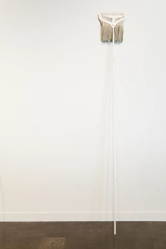 A white, long handled mop with discolored yarn leans upside down against a white wall.