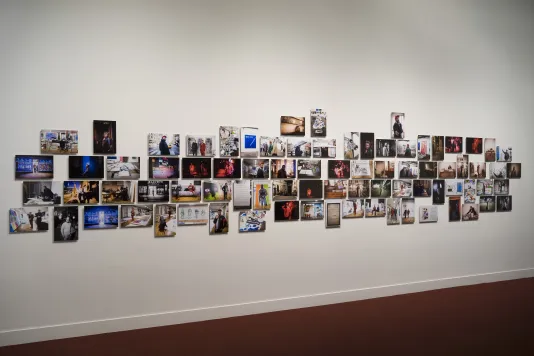A horizontal “salon-style” arrangement of approximately 160 color photographs hangs on a white gallery wall.