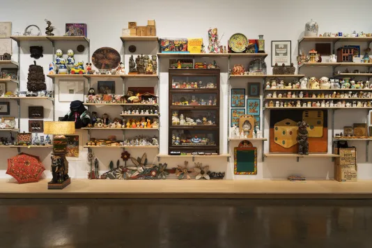 Ceramic, plastic and wood figurines; a painting of dice; framed artworks; vases; a small red umbrella fill shelves on a wall.