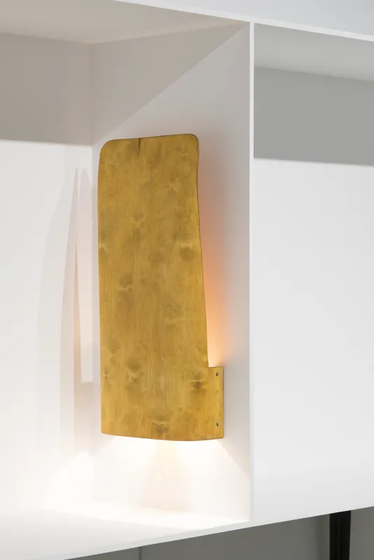 An illuminated lamp with a vertical wood shade is affixed to the middle vertical partition of a white shelf.