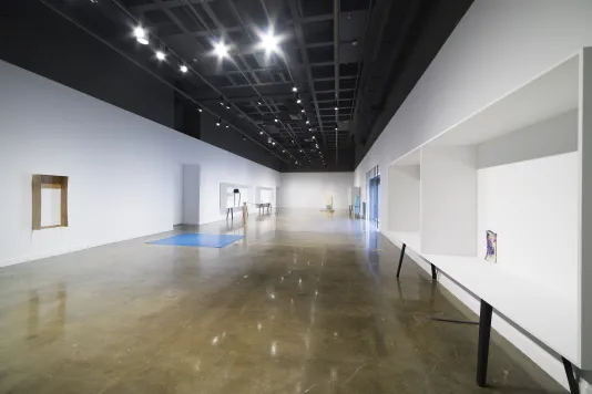 White display cases with black legs line both walls. A brown mounted sculpture is on the wall. A blue mat is on the floor.