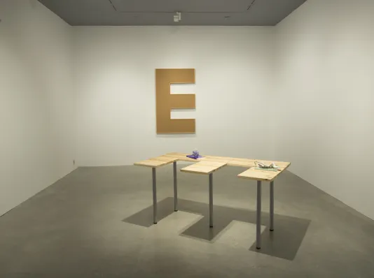 A gallery features two sculptures shaped like the letter "E" on the wall and as a table by Lina Viste Grønli.