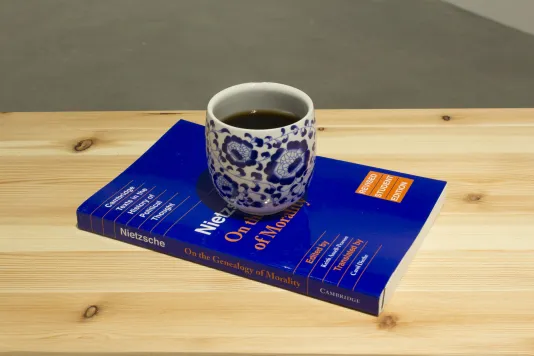 A cup with blue floral design filled with Coca Cola rests on a copy of Nietzche's "On the Genealogy of Morality".