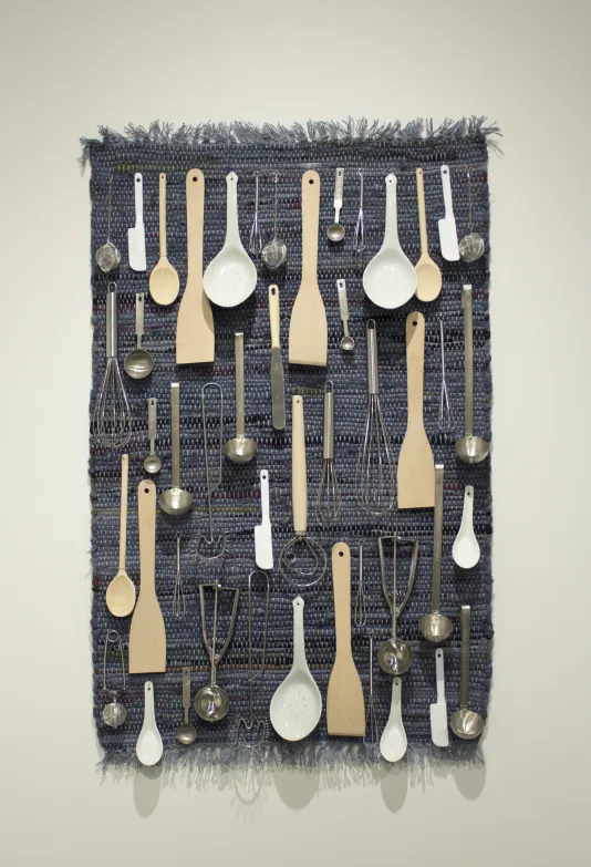 A blue tapestry adorned with silverware, whisks, and ladles.