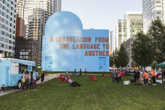 People on the green lawn in front of the blue façade with “A Translation From One Language To Another” painted in red.