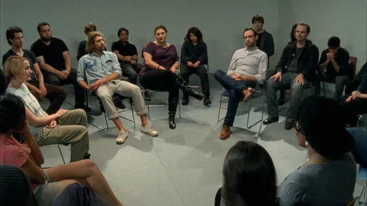 A group of young men and women sit in two concentric circles, listening to something with varying degrees of attention.
